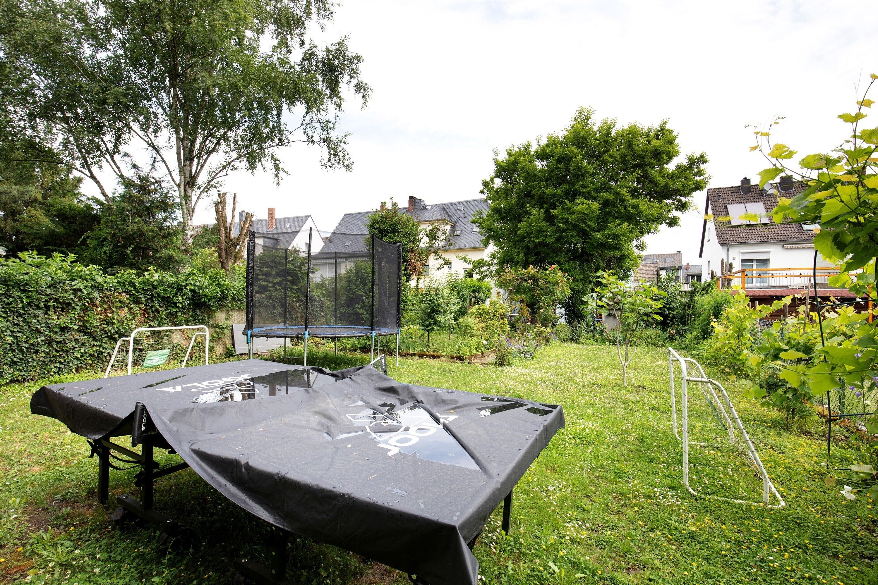 A covered table in a grassy outdoor area with a trampoline and a metal ladder.