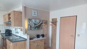 A kitchen with a sink, stove, and cabinets, a dining area with a table and fruit, and a door with a lock. - Apartment 9: Feel at Home Away from Home – Great Comfort with Wi-Fi & EV Charging Station (Altenau)
