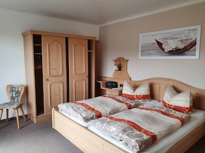 Une chambre à coucher avec un lit en bois, une armoire en bois, une chaise, une table de chevet avec une lampe et un tableau accroché au mur.