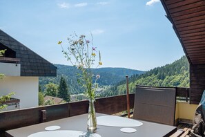 A balcony with a table, a vase with flowers, and a scenic mountain view.