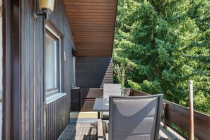 A wooden deck with outdoor furniture, a window, and a view of a dense forest.