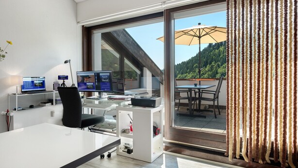 Ein modernes Büro mit Glaswand, Schreibtisch, zwei Bildschirmen und einem Stuhl.