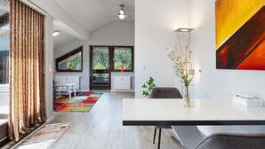 Ein modernes Interieur mit weißer Decke, einem Essbereich, einem großen Fenster und einem an der Wand hängenden abstrakten Gemälde.