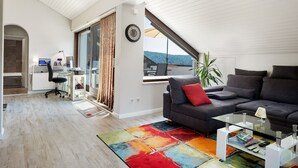 Ein modernes Wohnzimmer mit einem dunkelgrauen Sofa, einem Glastisch und einem farbenfrohen Teppich.