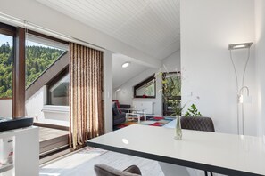 A modern living room with a large window, a dining table, and a sofa.