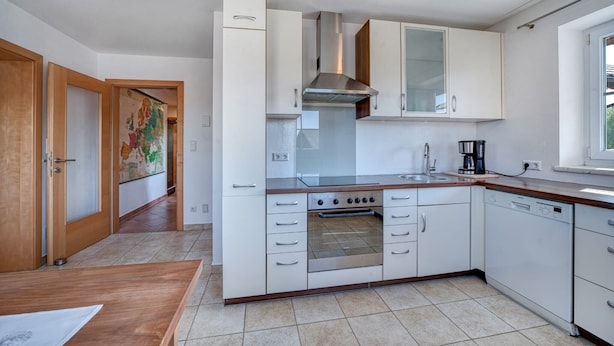 Una cocina moderna con armarios blancos, una campana extractora de acero inoxidable, horno empotrado y lavavajillas.