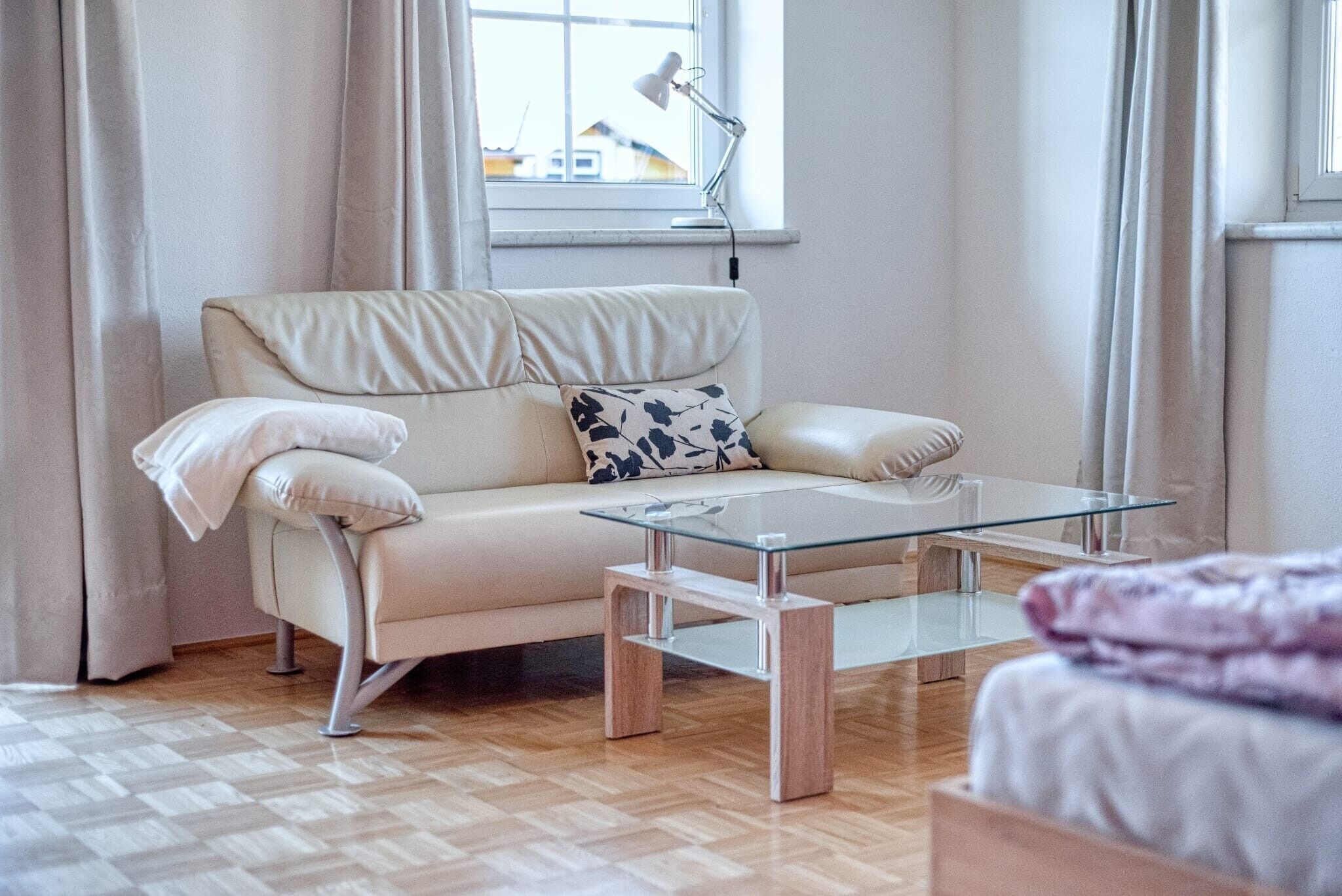 Una sala de estar moderna con un sofá color beige, una mesa de centro de vidrio y vistas al exterior a través de una ventana.