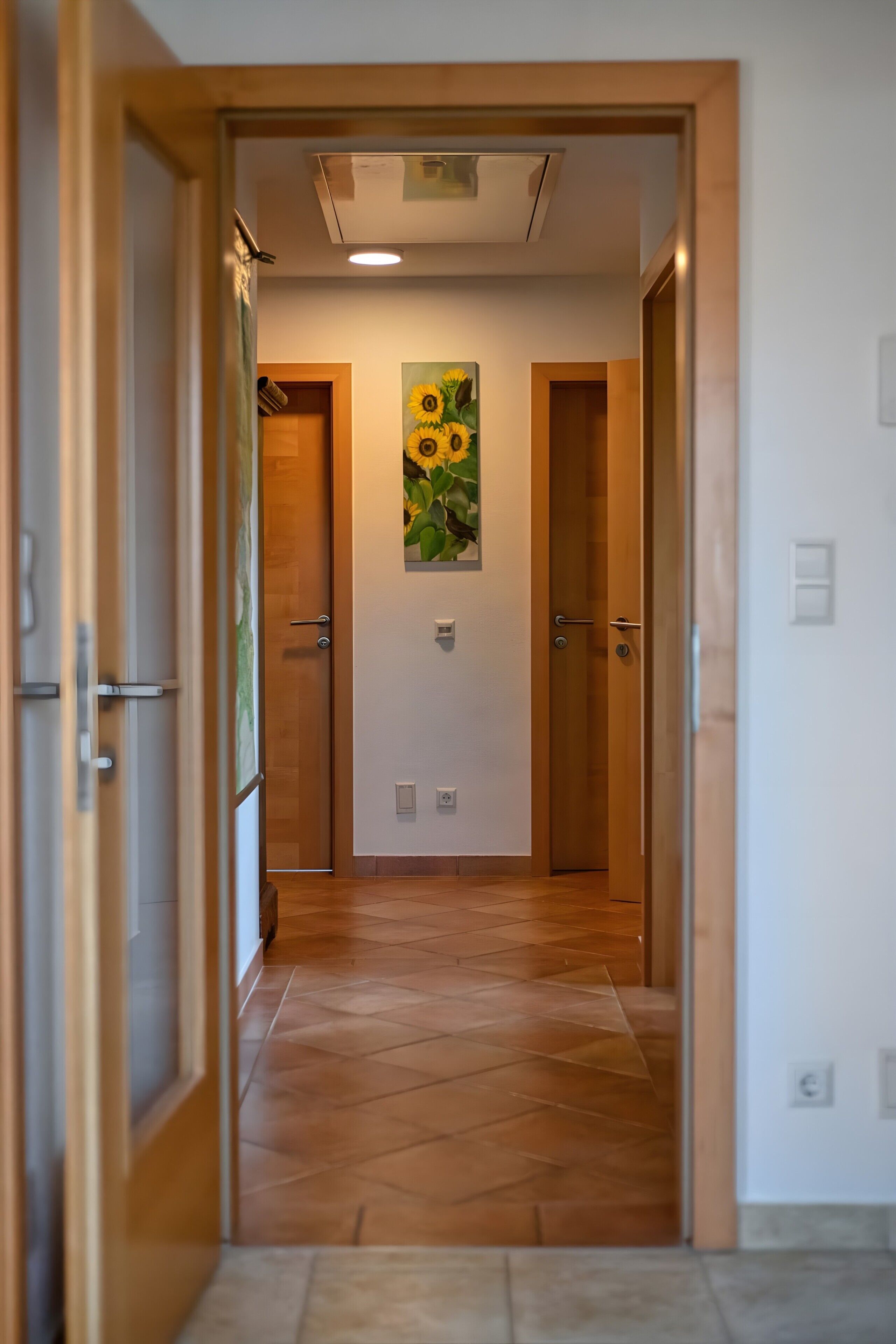 Um corredor com portas de madeira, chão de azulejos e um quadro de girassóis na parede.