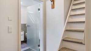 Un interior moderno con una puerta de cristal que da a un baño, una decoración de asta de ciervo en la pared, y una escalera con alfombra.