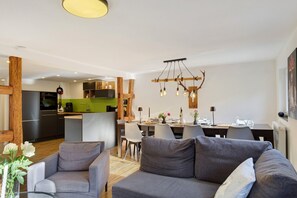 A modern living room with a grey sofa, a dining area with a table and chairs, a kitchen with a green backsplash, and a unique light fixture.