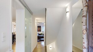 Un pasillo con puerta de vidrio, suelo de madera y escalera con espejo y cortina.