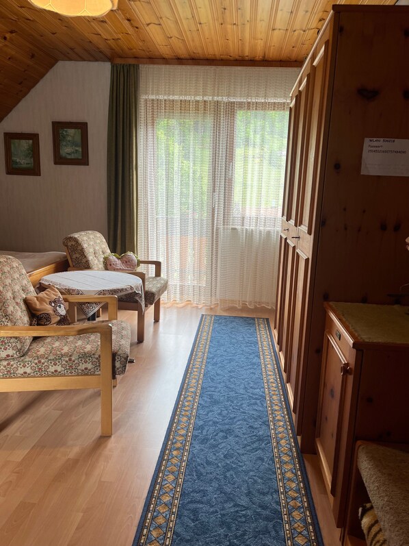 Una habitación acogedora con techo de madera, alfombra azul estampada, sofá, sillón y un aparador.