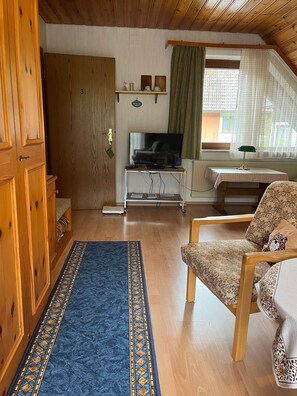 A wooden-paneled room with a television, a scale, a patterned rug, and a floral chair. - Room 'Doppelzimmer' with Shared Garden, Balcony and Wi-Fi (Bad Rippoldsau-Schapbach)
