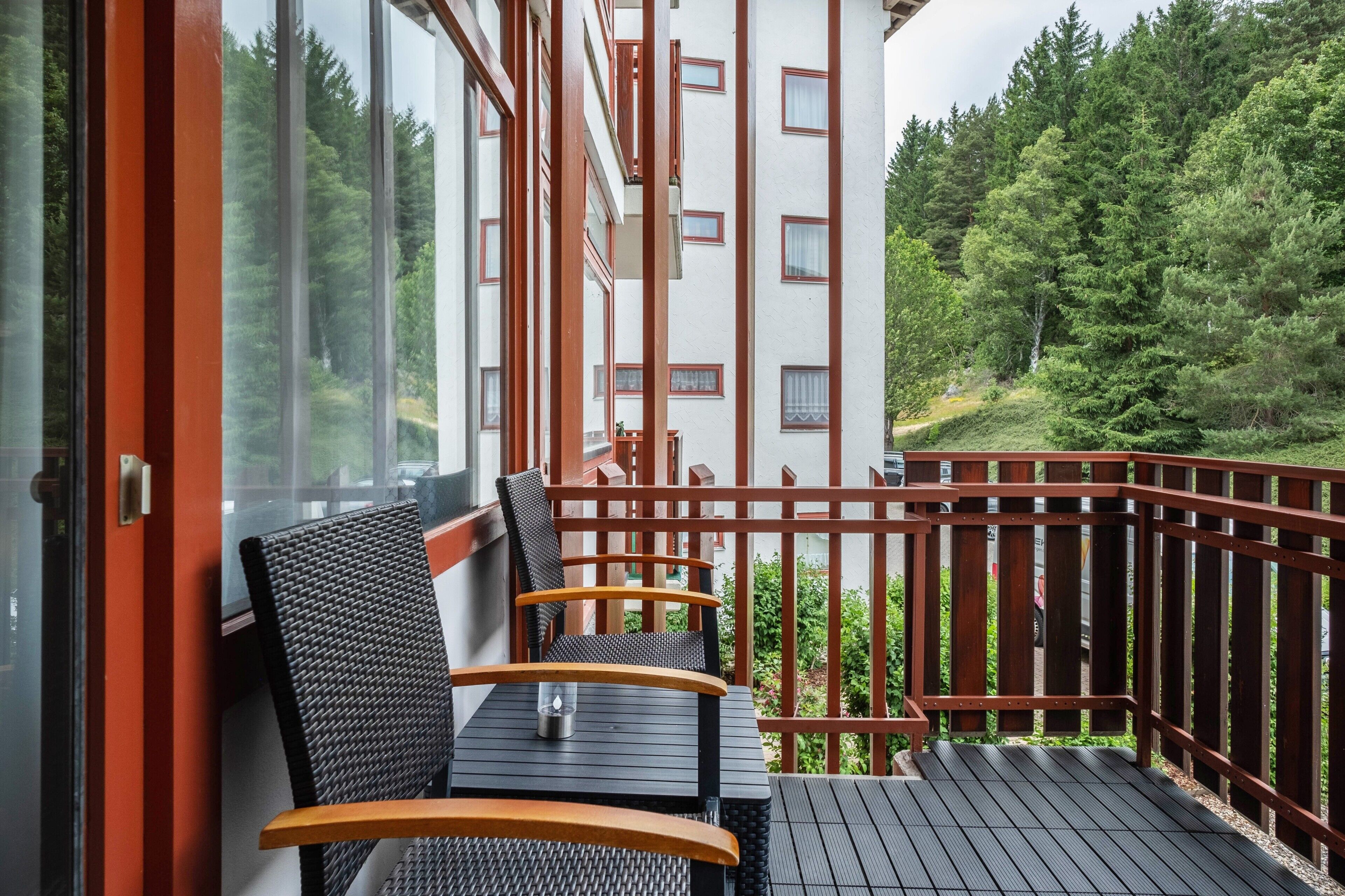 Ein Balkon mit zwei Stühlen und einem Tisch, mit Blick auf ein bewaldetes Gebiet.
