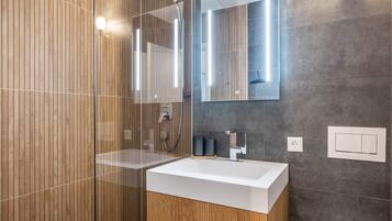 Ein modernes Badezimmer mit Duschkabine aus Glas, einem weißen Waschbecken und einem Spiegel mit integrierter Beleuchtung.