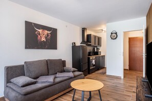 Un soggiorno con divano, un tavolo rotondo in legno, una cucina con pensili neri e un quadro raffigurante un toro.