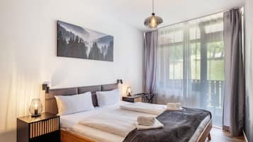 Ein Schlafzimmer mit Bett, Nachttischen, einer Lampe, einem Gemälde und Blick durch ein Fenster.