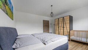 Une chambre à coucher comprenant un lit, un berceau, une armoire et un luminaire suspendu.
