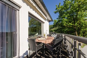 Ein Essbereich im Freien mit Tisch und Stühlen, Blick auf die umliegende Landschaft und ein Gebäude mit großen Fenstern.