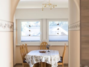 A dining area with a round table, chairs, a chandelier, and windows with blinds.