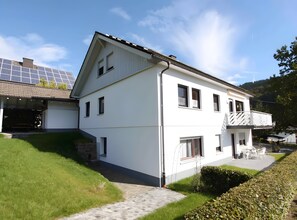 A white two-story house with a balcony, solar panels, and a stone chimney.