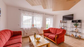 A living room with two red sofas, a wooden coffee table, a TV, and a bookshelf. - Holiday Apartment 'Dachsbau' with Private Terrace, Shared Garden and Wi-Fi (Schmallenberg)