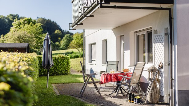 A house with a balcony, a table with a red tablecloth, and a garden area. - Holiday Apartment 'Dachsbau' with Private Terrace, Shared Garden and Wi-Fi (Schmallenberg)