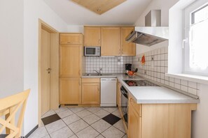 Una cocina compacta con armarios de madera, microondas integrado, extractor de acero inoxidable y una ventana que proporciona luz natural.