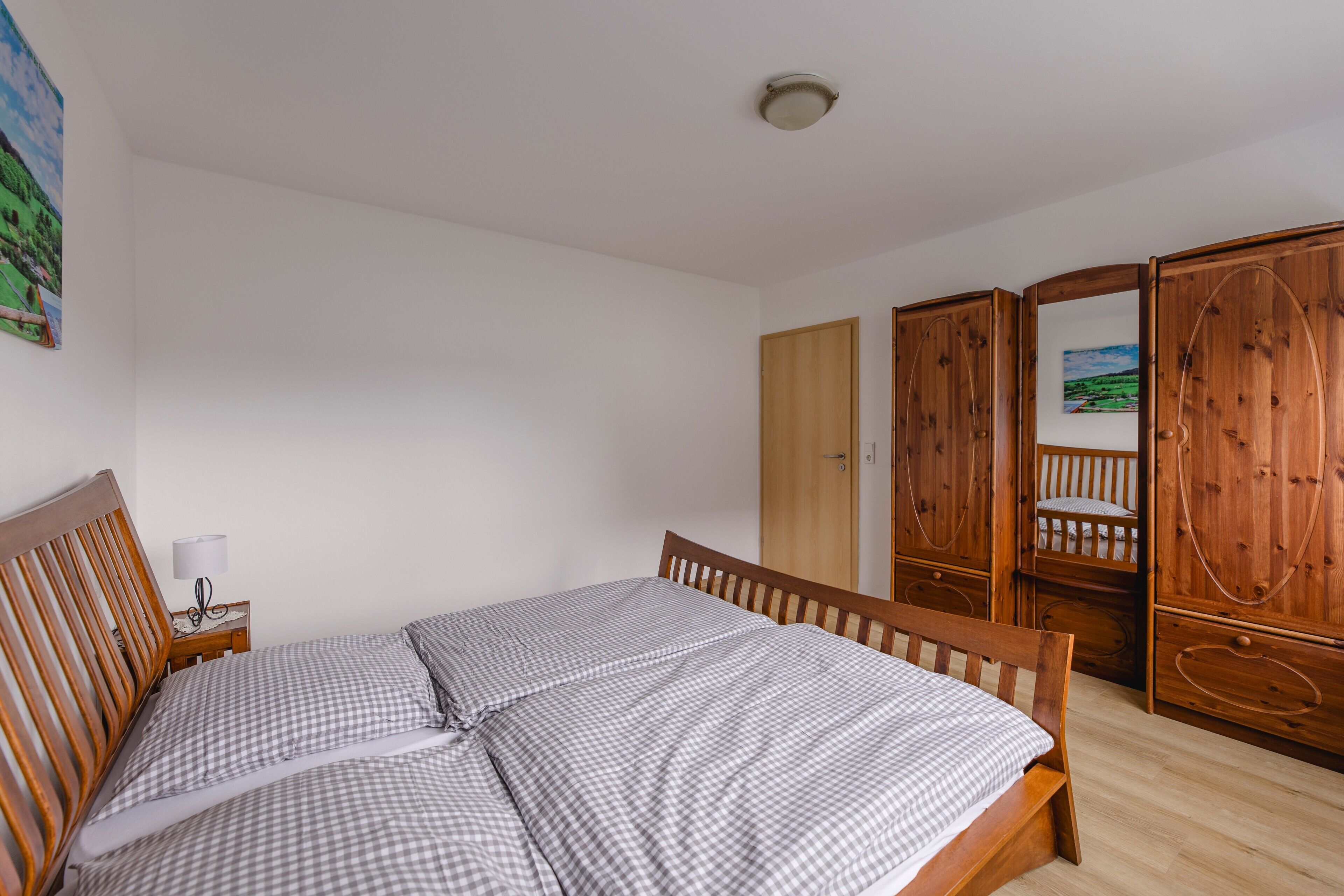 A bedroom with a wooden bed, a nightstand with a lamp, and wooden wardrobes.
