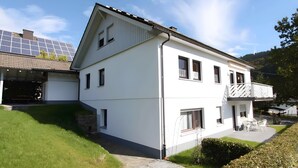 A white two-story house with a balcony, solar panels, and a stone chimney. - Holiday Apartment 'Dachsbau' with Private Terrace, Shared Garden and Wi-Fi (Schmallenberg)