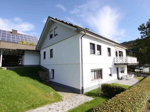 Um edifício branco de dois andares com varanda, painéis solares e entrada pavimentada.