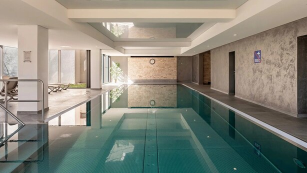 Una piscina interior moderna con paredes de vidrio transparente, piso de baldosas y diseño minimalista.
