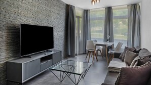 A modern living room with a flat-screen TV, a glass coffee table, a sofa, a dining table with chairs, and a large window with curtains. - Holiday Apartment 'Loft Style' with Balcony and Wi-Fi (Schluchsee)