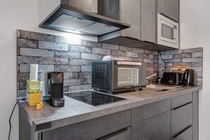 A modern kitchen with a stone backsplash, a built-in microwave, a coffee maker, and a Krups induction cooktop.