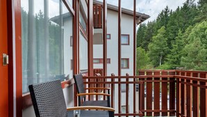 A balcony with a table and chairs, overlooking a forested area and a building with multiple windows. - Holiday Apartment 'Loft Style' with Balcony and Wi-Fi (Schluchsee)