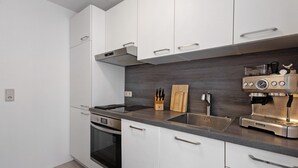 Eine moderne Küche mit weißen Schränken, einer Edelstahl-Espressomaschine und einem Holzer Schneidebrett.