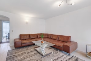 Una sala de estar moderna con un sofá de cuero marrón, una mesa de centro de vidrio y una alfombra estampada.