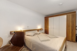 Un dormitorio con cama, mesita de noche, silla, armario y lámpara.