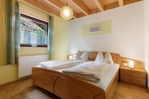 Une chambre à coucher avec un lit en bois, une table de chevet, une fenêtre avec des rideaux et un tableau accroché au mur.