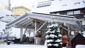 Un'area salotto all'aperto riparata, con sedie e un tavolo, un albero imbiancato dalla neve e un edificio con tetto spiovente sullo sfondo.