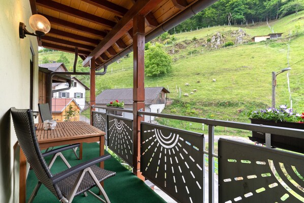 Un balcon avec une table et des chaises, une vue sur un paysage verdoyant et une maison en arrière-plan.