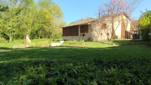 Ein rustikales Steinhaus mit Ziegeldach, umgeben von einer gepflegten Rasenfläche und Bäumen.