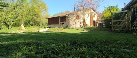 A rustic stone building with a tiled roof, surrounded by a well-maintained grassy area and trees.