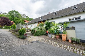 Rua residencial com casas, plantas em vasos e uma bicicleta.