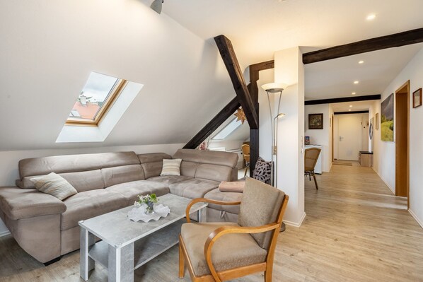Un loft moderno con un amplio sofá modular, una silla de madera, una mesita y un tragaluz.