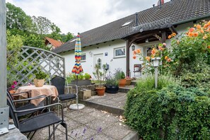 Um pátio com área de estar externa, vasos de plantas e uma casa com telhado em telhas.