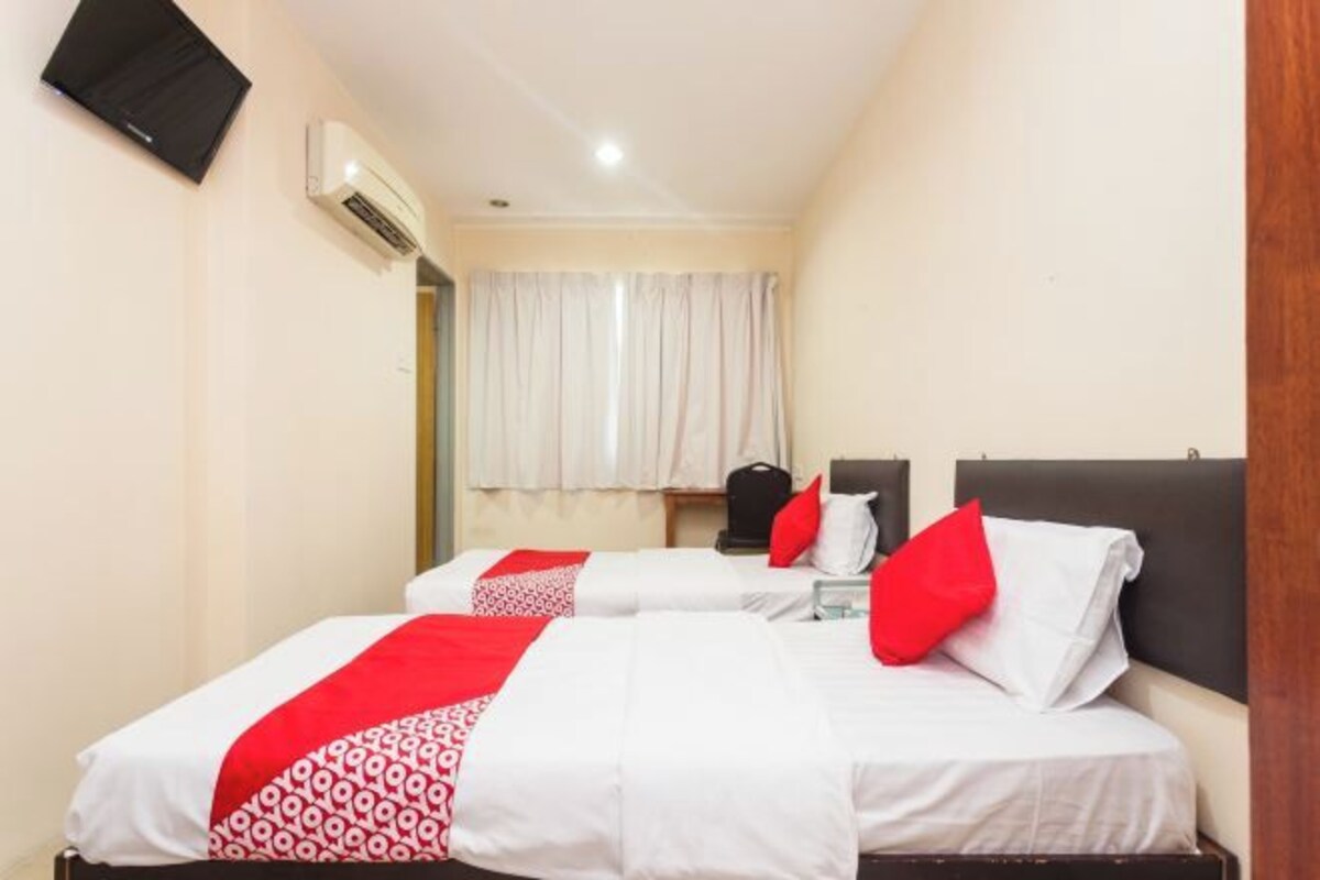 Habitación de hotel con dos camas, un televisor de pantalla plana montado en la pared y una ventana con cortinas.