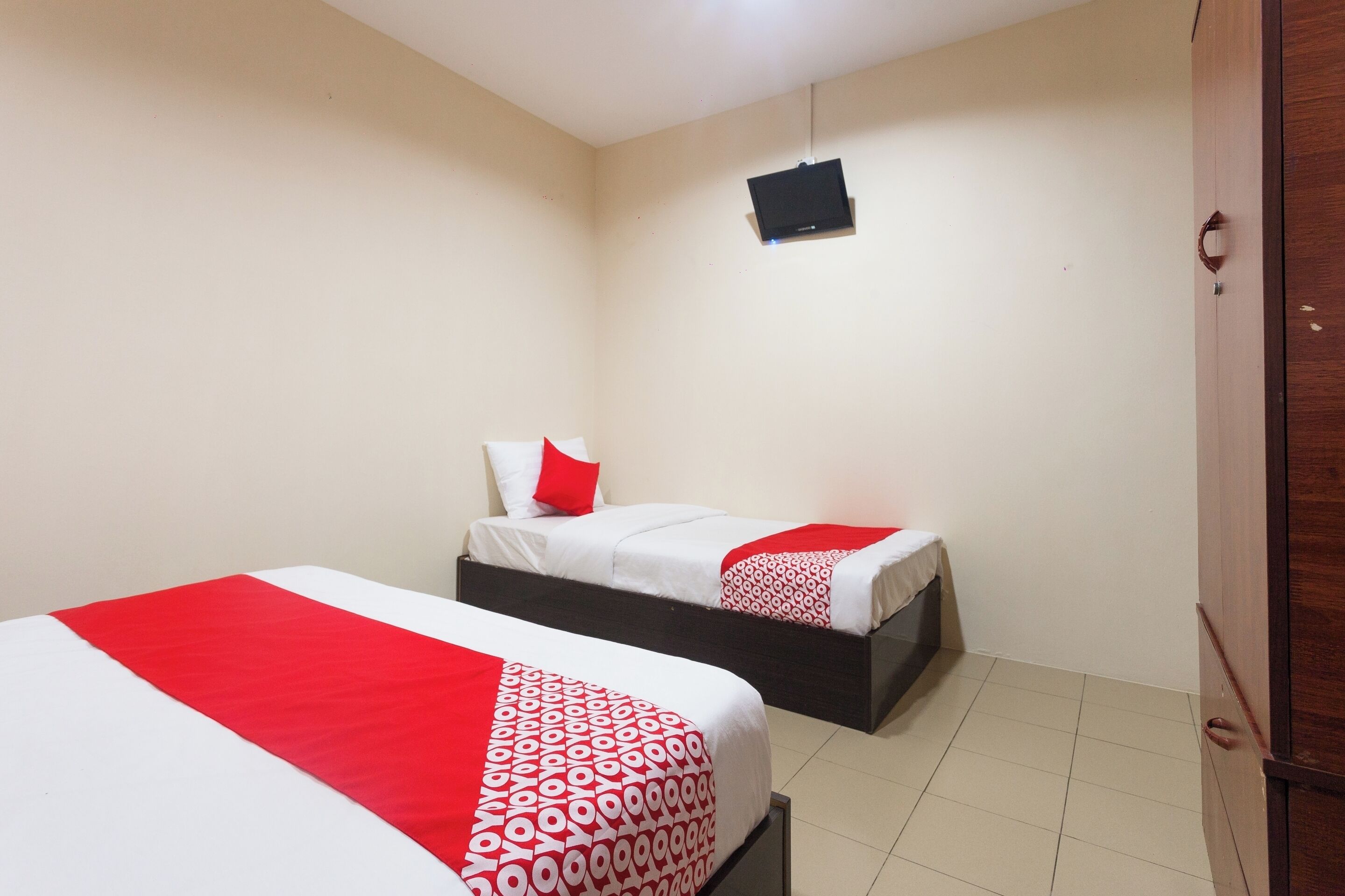 Habitación de hotel con dos camas, cada una con una colcha roja y blanca, un televisor pequeño en la pared y un armario de madera.