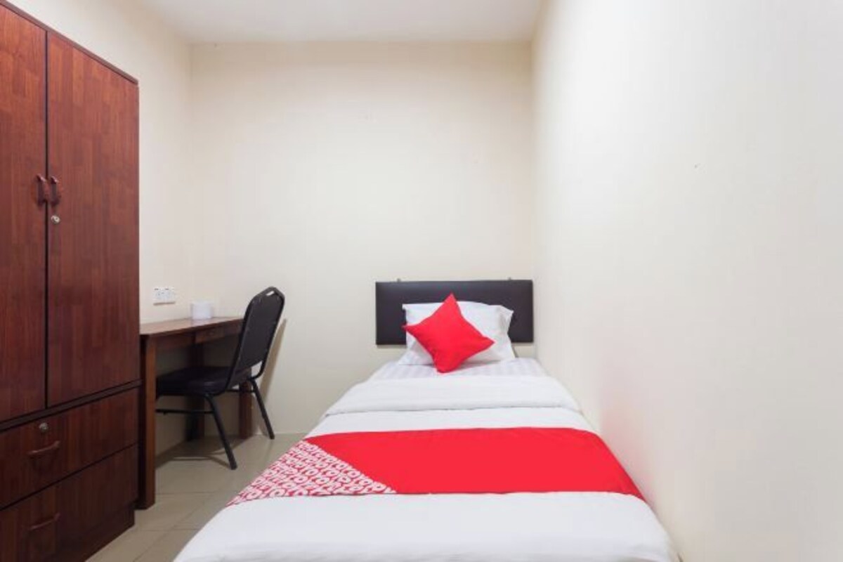 Una habitación pequeña con una cama individual, un armario de madera, un escritorio con silla y una colcha roja y blanca.