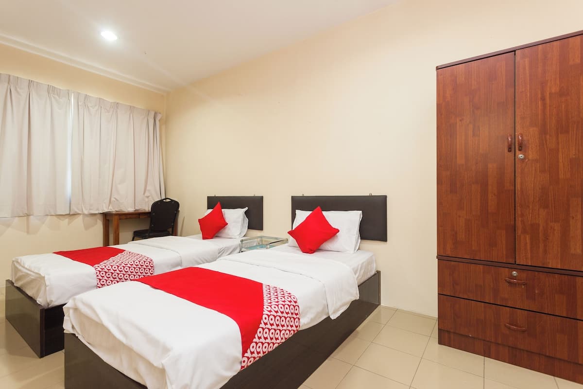 A hotel room with two beds, a wardrobe, a window with curtains, and a small table with a chair.